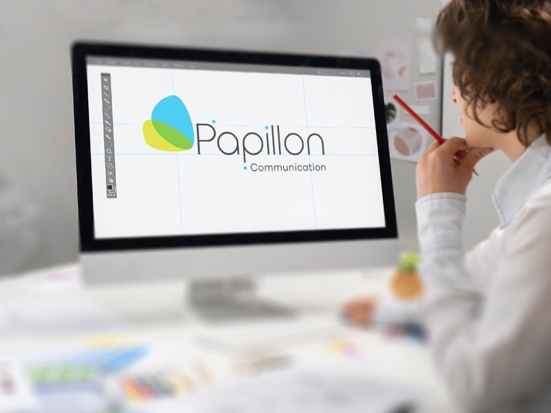 La Graphiste en réflection. Photo d'une graphiste en action devant son ordinateur où est affiché le logo Papillon Communication.